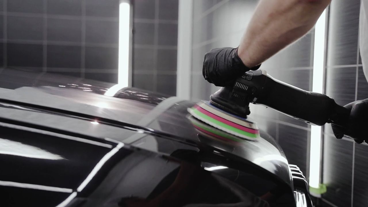 Stock photo: a gloved hand polishing black car paint with a small machine polisher