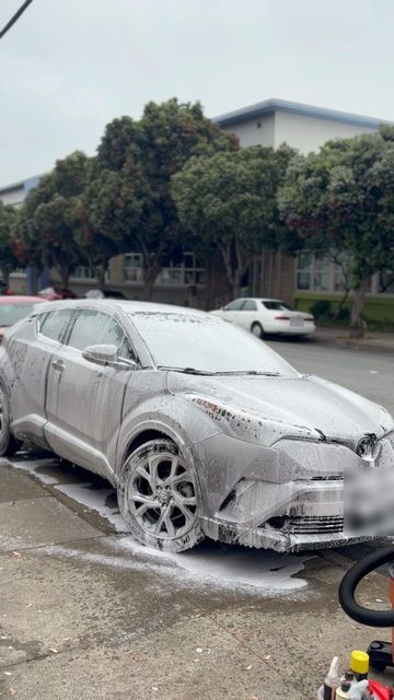 Silver Toyota C-HR covered in snow foam, parked at a curb