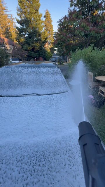 Snow foam sprayed over the hood and windshield of a dark BMW in a garden driveway