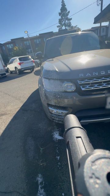 Pressure washer wand rinsing foam off the front of a Range Rover Sport in a parking lot
