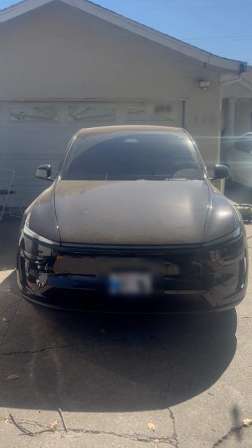 Black Tesla Model Y in a driveway with a dusty, dull hood before washing