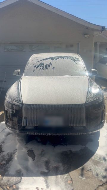 Black Tesla Model Y covered in white snow foam in a driveway